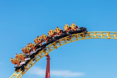 Rusya, Soçi 14.05.2022. Yolcularla dolu lunapark treni mavi gökyüzüne doğru sarı ray boyunca koşuyor.