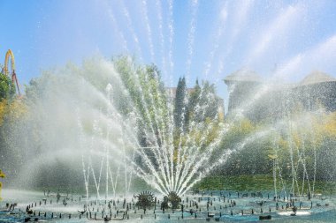 Fıskiyenin serpintisi, güneşli bir günde, park mimarisinin ve mavi gökyüzünün arka planına karşı yelpaze şeklinde dağılıyor..