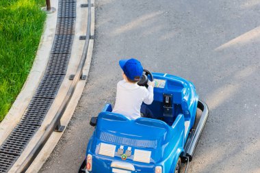 Mavi şapkalı bir çocuk park yolu boyunca mavi minyatür çocuk arabası kullanıyor. Lunaparktaki çocuk turları. Çocuklar için karting