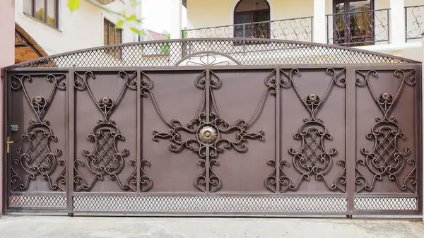 Patterned expensive iron fence of private household. Villa entrance. Production of forged doors. Reliable property protection.