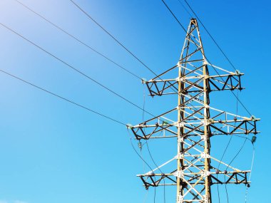 Aydınlık bir günde mavi gökyüzünün altında güneş tarafından aydınlatılan kablolarla elektrik direği