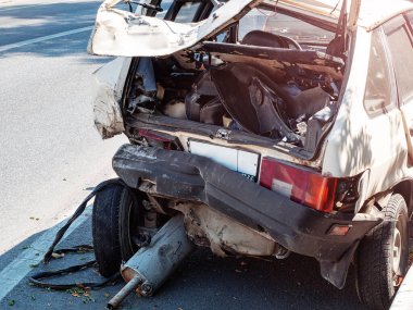Güneşli bir günde yolun kenarında egzoz borusu düşmüş, hurda ve buruşuk bir araba.
