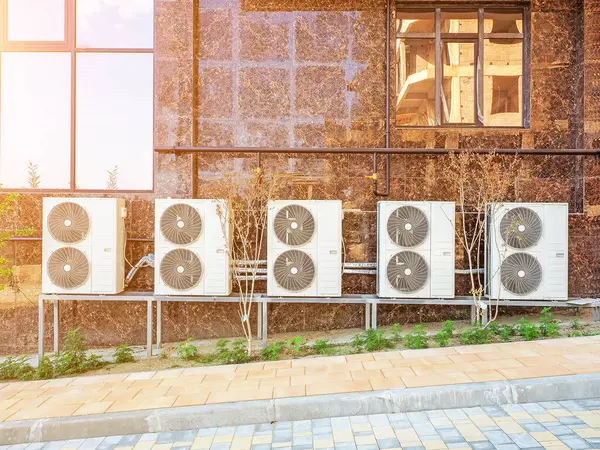 A row of double industrial air conditioners is mounted on a brown marble tiled wall. View outside.