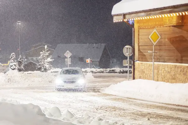 The car is driving down the night street in the snow