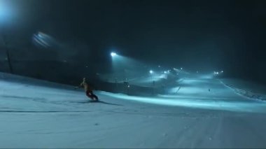 Kar fırtınasında gece kayağı. Gece kayak pistinde kayak yapmak. Gece çekimi. Hareket halindeyken ateş ediyorlar. Bir snowboardcuyla çarpıştı.