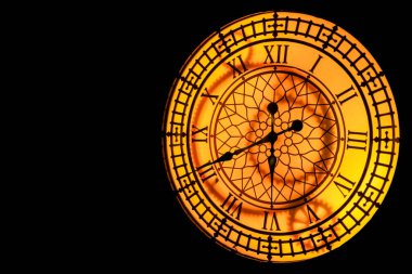 Koyu bir duvarda asılı sarı turuncu saat.