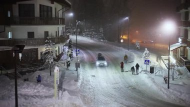 Rusya, Sochi Roza Khutor 22.12.2021. İnsanlar kar yağarken gece sokakta yürürler.