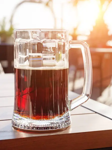 Mug of dark beer on wooden table outdoor cafe. Half empty beer mug. Selective focus.