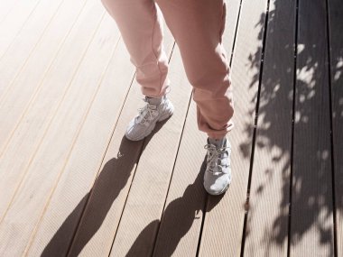 Bahar güneşiyle aydınlatılan verandanın ahşap zemininde bir kadın duruyor..