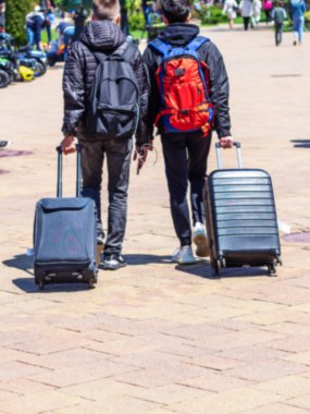 Tekerlekli bavullarla yürüyen iki adam. Erkeklerin sırtında sırt çantaları vardır..