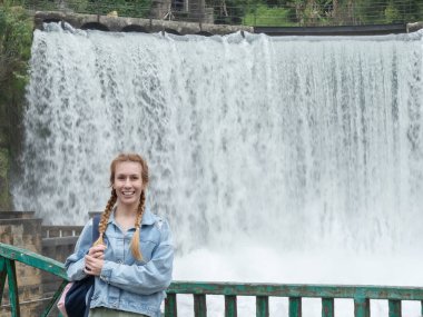 Geniş şelalenin önünde gülümseyen kadın. Büyük şelalenin yanındaki turist