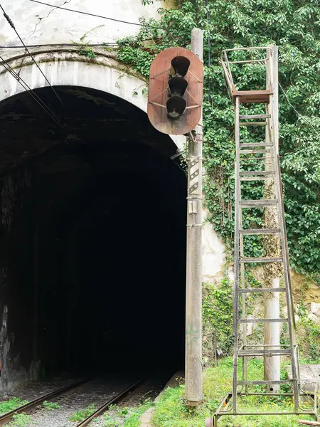 Entrance to a dark railway tunnel. Rusty railway abandoned traffic light.