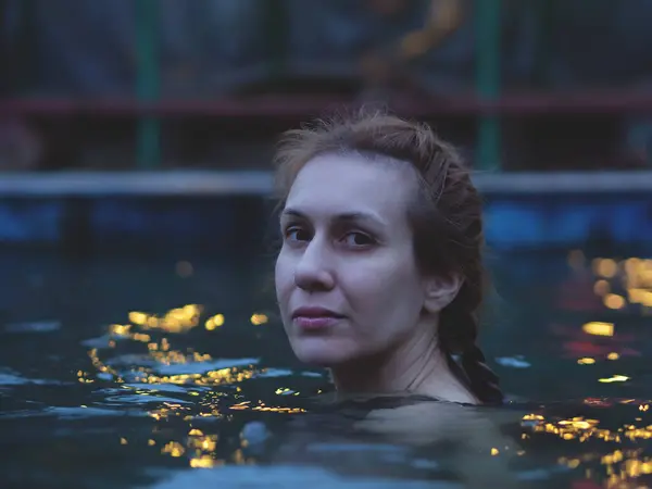 Woman swims in shimmering water outdoors. Evening swim in the mineral pool