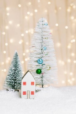 Noel ve Yeni Yıl minyatür evi. Karda süslü ağaçlar var. Arka planda sıcak ışıkları olan küçük bir oyuncak ev. Noel süsleri. Tatil ve kutlama konsepti.