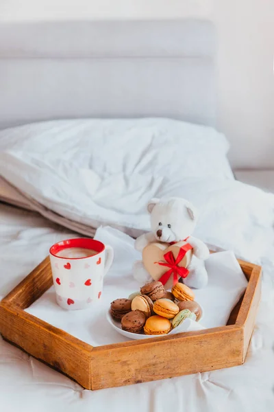 Ημέρα του Αγίου Βαλεντίνου πρωινό στο κρεβάτι για τον εραστή. Αρκουδάκι με κουτί δώρου σε σχήμα καρδιάς με κόκκινη κορδέλα, ένα φλιτζάνι καφέ και μπισκότα αμυγδάλου στο ξύλινο δίσκο. Ρομαντικό πρωινό. Κάθετα. Αντιγραφή χώρου — Φωτογραφία Αρχείου
