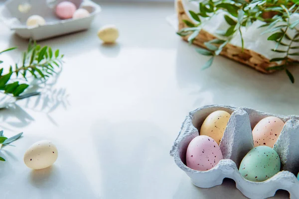 Easter holoday background with copy space. Multicolored painted eggs in a cardboard box, fresh green branches and straw basket with festive pastry on white kitchen table. Selective focus. Copy space — Φωτογραφία Αρχείου