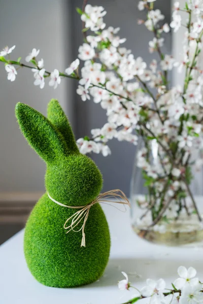 Grüner Osterhase mit blühenden Blumen auf Zweigen in der Vase auf dem weißen Tisch. Frohe Ostern Frühling vertikale Karte. Selektiver Fokus — Stockfoto