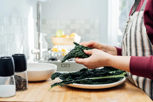 Woman tearing curly green kale leaves into pieces for kale, chips or salad. Healthy eating cooking step, ready to prepare food. Selective focus, copy space. — Stock Photo, Image