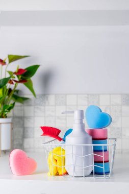 Oda servisi konsepti. Yıkama sabunu, kalp şeklinde süngerler, sepetteki fırça ve peçeteler yeşil bitkilerle. Dikey kart. Seçici odaklanma. Boşluğu kopyala.