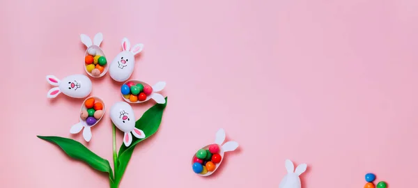 Vista superior Fondo rosa de Pascua con forma de flor hecha de contenedores de huevos divertidos con orejas de conejo llenas de huevos de chocolate dulces. Conejo símbolo de conejo. Caza de huevos de Pascua. Pascua creativa. Banner ancho. —  Fotos de Stock