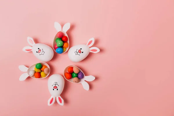 Oster-rosa Hintergrund mit Blütenform aus lustigen Eierbehältern mit Hasenohren gefüllt mit Schokoladeneiern. Hasen-Symbol. Ostereiersuche. Kreative Ostern. Kopierraum. — Stockfoto