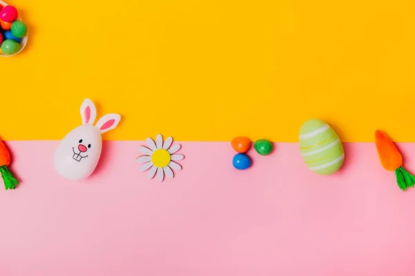 Vista superior festiva Pascua rosa y amarillo fondo con huevos de colores, zanahorias decorativas, conejos, flores, huevos de chocolate. Pascua brillante creativa. Acostado. Copiar espacio. — Foto de Stock
