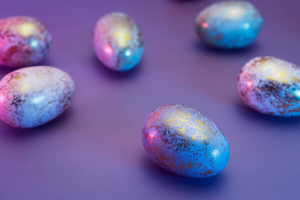 Easter golden eggs with different patterns in neon colors light. Purple very peri color minimalist festive background. Modern trendy Easter. Selective focus. Copy space.