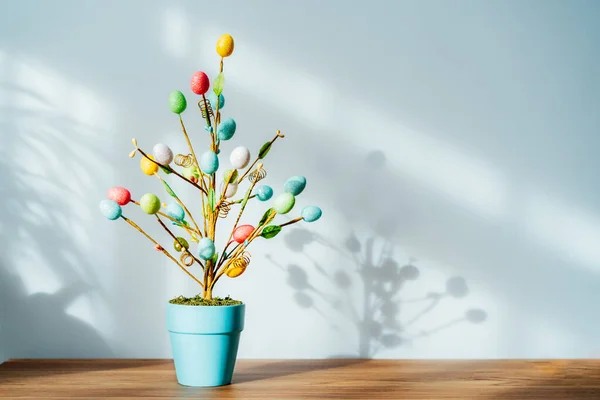 Decoración del árbol de Pascua en maceta azul con huevos de colores en la consola de madera con luz y fondo de sombra. Decoración de la casa de Pascua. Minimalismo, estilo escandinavo. Enfoque selectivo. Copiar espacio. — Foto de Stock