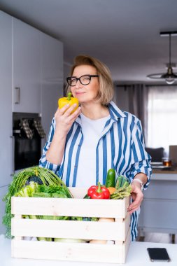 Tahta kutudan taze sebzelerle taze organik dolmalık biber alan bir kadın. Yerel çiftçi sağlıklı yiyecekler. Sağlıklı bir hayata yeni bir başlangıç, kilo verme kavramı. Çevrimiçi ev yemeği servisi. Dikey kart.