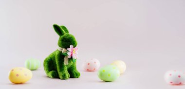 Yeşil tavşan heykelciği ve renkli paskalya yumurtaları tarafsız pembe arka planda farklı şekillerde. Bayramlık Ester bahar kartı modeli. Afiş geniş. Seçici odaklanma. Boşluğu kopyala.