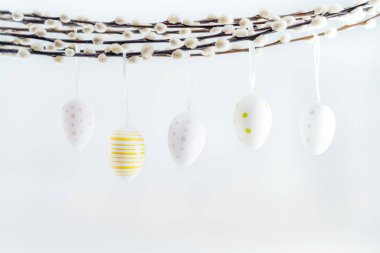 Blooming pussy willow branches and hanging on it easter eggs in different patterns on the white background. Minimalist, Modern Happy easter card. Selective focus, copy space.