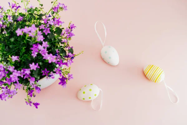 Ein Strauß lila Frühlingsblumen im Topf und bemalte Ostereier auf hellrosa Hintergrund. Flache Lay festlichen Hintergrund. Selektiver Fokus. Kopierraum — Stockfoto