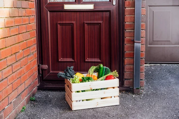 Contactless home fresh food delivery. Wooden box with vegetables and fruits standing near house entrance door. Support local farmer food production. Online food order. Recipe box. Copy space. — Stock Photo, Image
