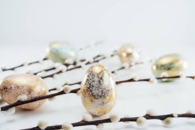 Blooming pussy willow branches and golden eggs in different patterns and colors on the white background. Minimalist, Modern Happy easter card. Selective focus, copy space.