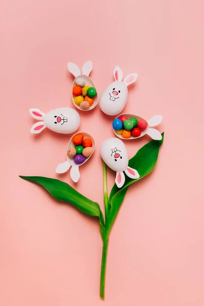 En üstteki Paskalya pembe arka planı, çiçek şeklinde yumurta kapları ve çikolatalı yumurtalarla dolu tavşan kulakları. Tavşan sembolü. Paskalya yumurtası avı. Yaratıcı Doğu.Dikey Kart. — Stok fotoğraf
