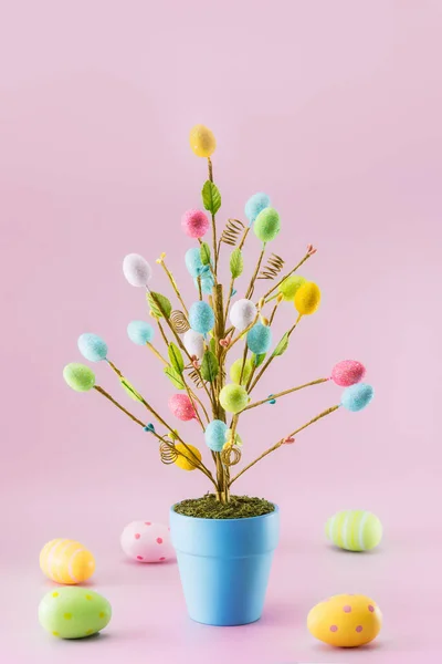 Decoración del árbol de Pascua en maceta azul con huevos de colores alrededor en el fondo rosa claro. Fondo festivo minimalista. Moderna maqueta de tarjeta de Pascua de moda. Tarjeta vertical. Enfoque selectivo. Copiar espacio — Foto de Stock