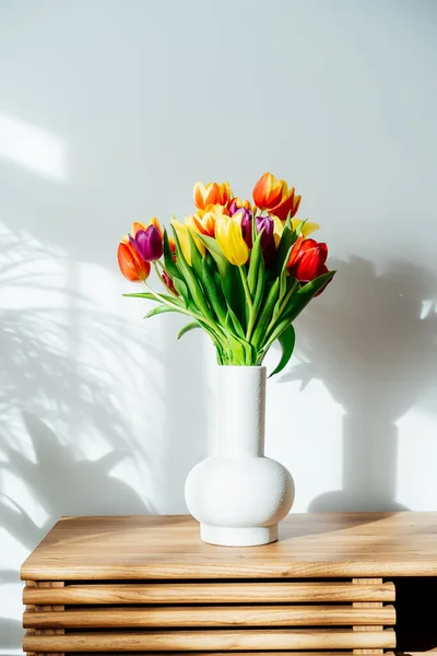 스칸디나비아 인들의 가정 내부에는 봄에 목조 캐 비넷 위에 서 있는 도기에 아름다운 튤립 꽃들 이 꽃다발을 이루고 있다. 녹색 식물 과흰 벽을 가진 광물 주의적 인 디자인이죠. 생물 애증 스타일이야. 봄철. — 스톡 사진