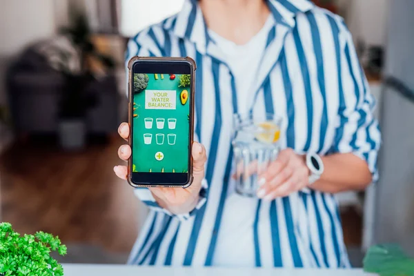 Su içmek için sağlıklı bir alışkanlık. Bulanık bir kadın limon kaplı bir bardak suyla vücut sıvısını kontrol etmek için aktif mobil uygulamalı bir telefon ile su dengesini takip ediyor. Seçici odak.