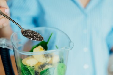 Mutfakta smoothie yaparken chia tohumu ekleyen kadını kapatın. Süper gıda takviyesi. Sağlıklı detoks vegan diyeti. Sağlıklı beslenme, kilo verme programı. Seçici odaklanma. Boşluğu kopyala.