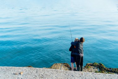 Çocuklar balık tutuyor. Arkadan bakan çocuk, kardeşine ya da arkadaşına balık tutmayı öğretiyor. Denize nasıl fırlatılacağını gösteriyor. Arkadaşlık ve kardeşlik kavramı. Çocuklar için açık hava aktivitesi. Seçici odak.