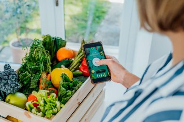 Üst görüşlü kadın elinde taze sebzeli ahşap kutu ve aktif online mobil uygulamalı vejetaryen diyet programı olan bir telefon tutuyor. Sağlıklı bir yaşam tarzının yeni başlangıcı, kilo verme kavramı.