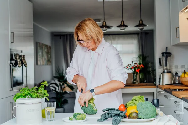 Femme d'âge moyen coupant le brocoli tout en cuisinant un plat sain pour le déjeuner sur la cuisine. Mode de vie sain. Cuisiner à la maison. Préparez la nourriture. Régime végétarien et végétalien. Concentration sélective. — Photo