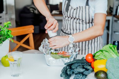 Yeşil kuşkonmaz tarifli fırında somon. Üçüncü adım. Somon ve sebzelere baharat ve tuz ekleyen bir kadın. Adım adım tarif et. Tarife göre evde sağlıklı yemekler.