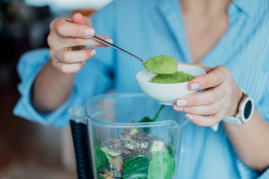 Mutfakta smoothie yaparken çimen tozu ekleyen kadını kapatın. Süper gıda takviyesi. Sağlıklı detoks vegan diyeti. Sağlıklı beslenme, kilo verme programı. Seçici odak