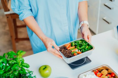 Kilo vermek için sağlıklı bir diyet planı, günlük hazır yemek menüsü. Beslenme çantasını önceden tartmış, mutfak terazisinde yemeye hazır bir kadın. Sağlıklı yemekle dengeli porsiyon. Pişirme öncesi konsept.
