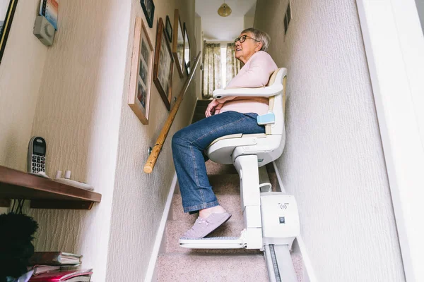 Mujer mayor que usa elevador automático de escaleras en una escalera de su casa. Escalera médica para personas con discapacidad y personas mayores en el hogar. Enfoque selectivo. —  Fotos de Stock