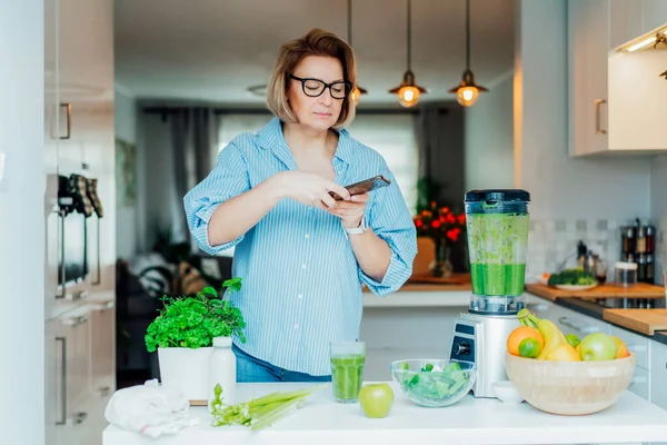 Blogueur créant du contenu pour les médias sociaux. Femme faisant photo, vidéo avec juste fait verre de smoothie vert détox et ses ingrédients sur la table de cuisine. Régime alimentaire sain, cuisine, blog de perte de poids — Photo