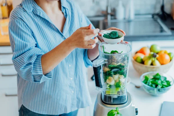 Femme ajoutant de la poudre verte de spiruline lors de la fabrication de smoothie vert sur la cuisine. Complément alimentaire. Alimentation végétalienne saine de désintoxication. Une alimentation saine programme de perte de poids. Concentration sélective. — Photo