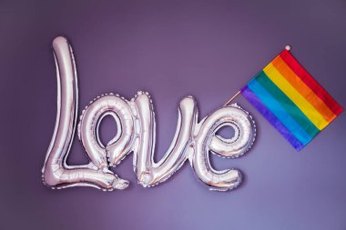 Mor arka planda LGBTQ gökkuşağı bayrağı olan gümüş folyo balonun aşk sözcüğü. Mutlu Gurur Ayı. Farklı aşk türlerinin beyanı. LGBT hakları. Seçici odak