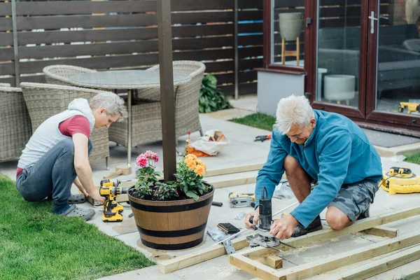 Adult son and father carpenter working together, handle wooden timbers in the garden. Patio construction by your own. DIY, Do it yourself. Home renovation, improvement, refurbishment. Selective focus.